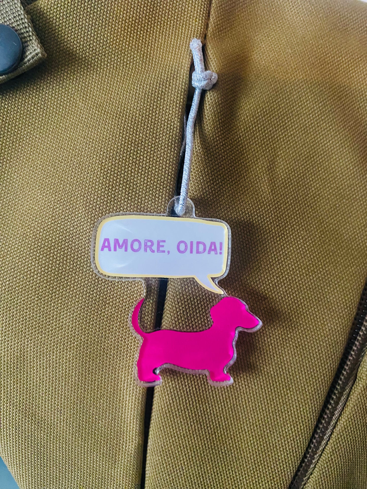 Anhänger in Form eines Dackels in pink mit Sprechblase, durch eine Schnur an einem reißverschluß befestigt.