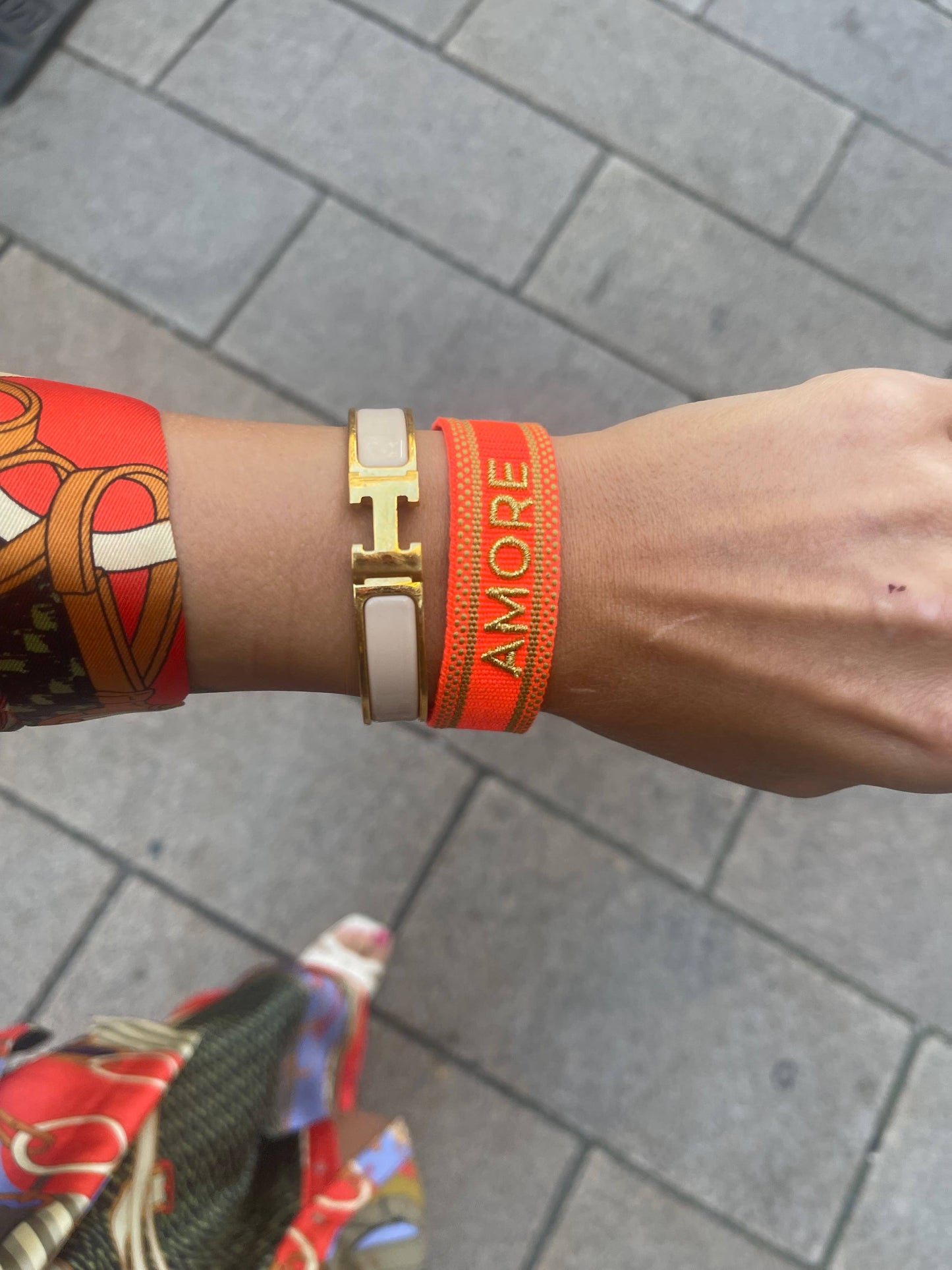 Gewebtes Armband in orange mit goldener Aufschrift "Amore" auf am Handgelenk einer Frau mit farblich passender Kleidung