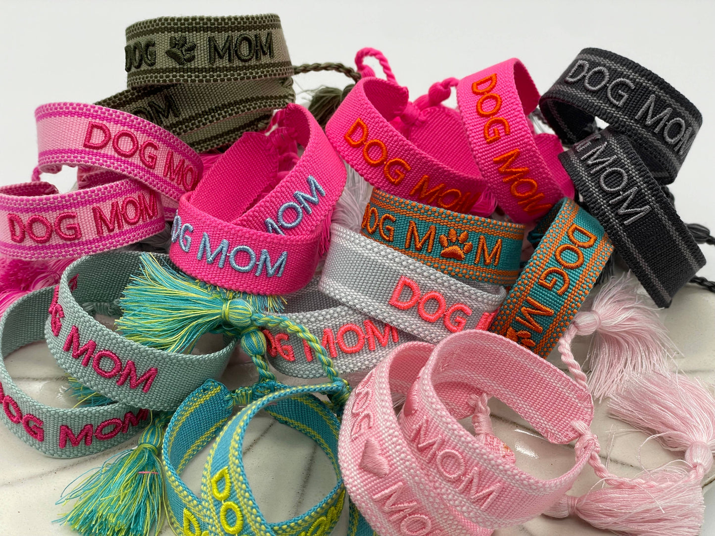 Mehrere Armbänder mit der Aufschrift "DOG MOM". Die Armbänder haben viele unterschiedliche Farben und sind in anderen Farben beschriftet.