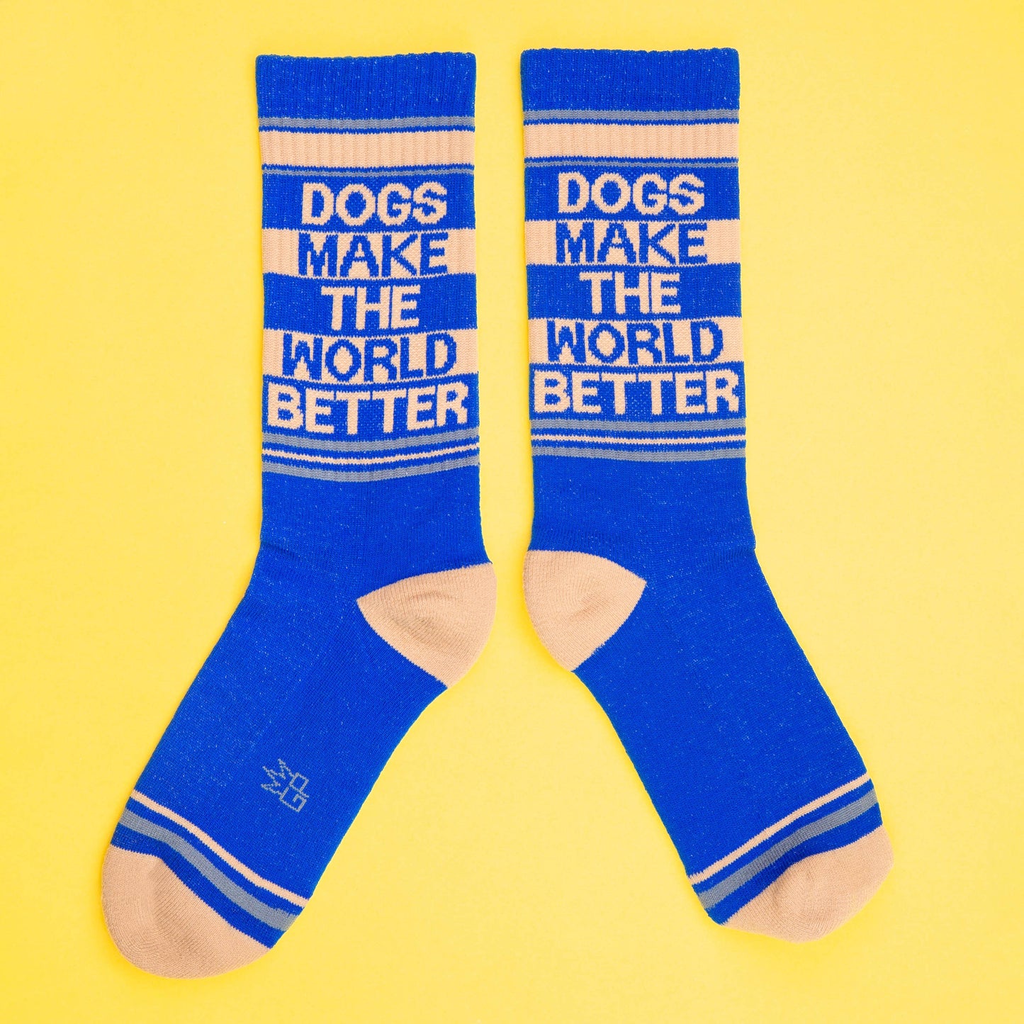 Ein Paar Socken in blau und beige. Die Aufschrift sagt Dogs make the world better. Die Socken zeigen nach links und rechts und sind auf gelbem Hintergrund abgebildet.