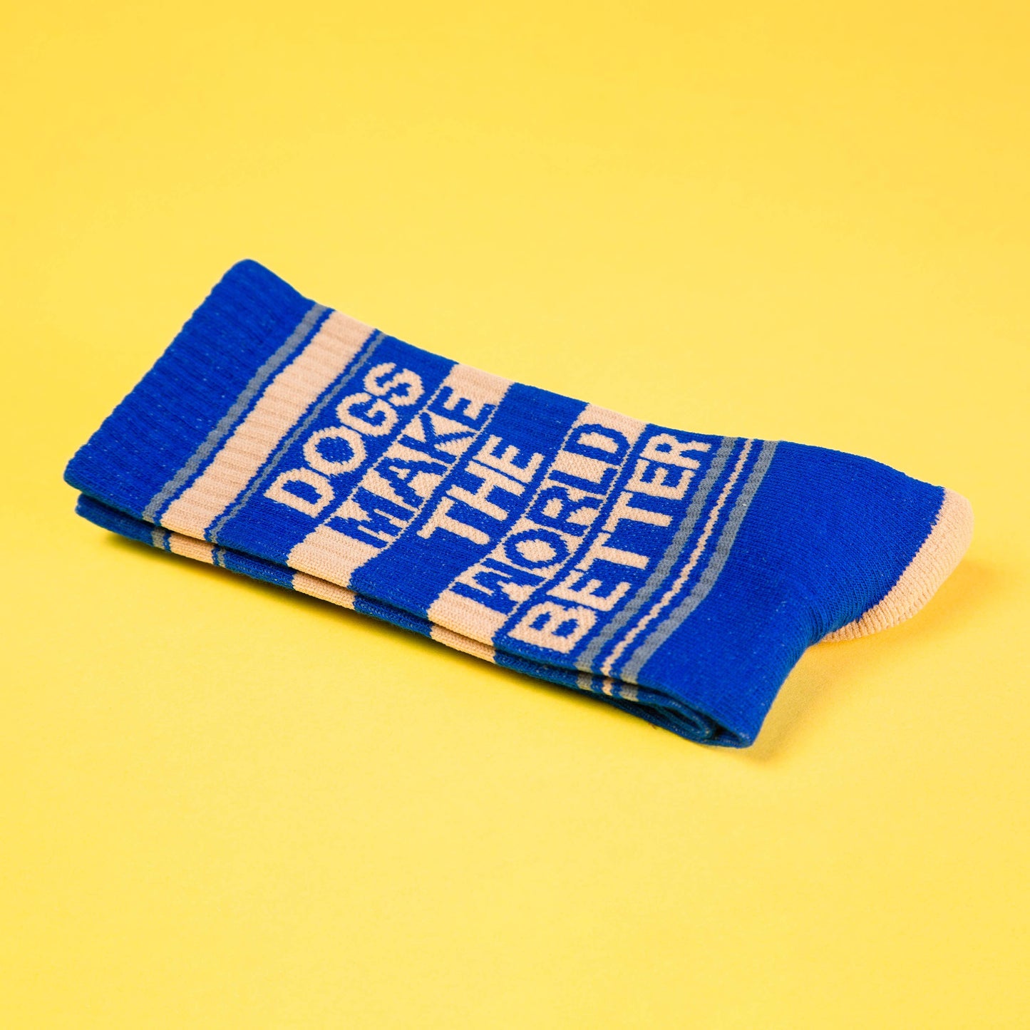 Ein Paar Socken in blau und beige. Die Aufschrift sagt Dogs make the world better. Die Socken liegen zusammengelegt auf einem gelbem Untergrund.