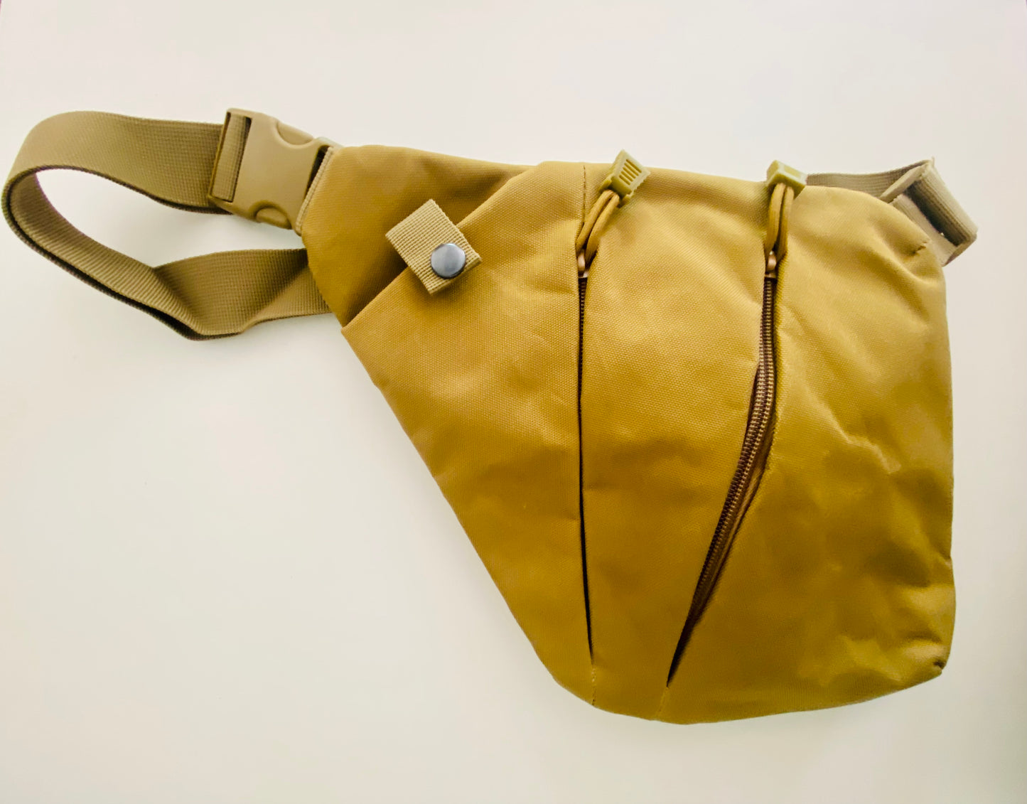 Tasche aus Canvas Stoff in oliv. Die Tasche hat zwei Reißverschlüsse und ein Fach, das mit einem Koopf verschlossen ist.