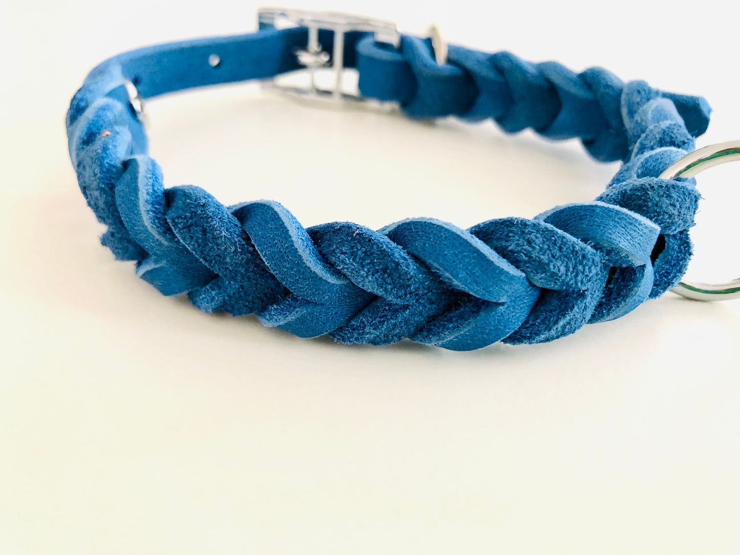 Ein blaues, geflochtenes Fettlederhalsband mit silberner Schnalle und Metallring, auf hellem Untergrund.