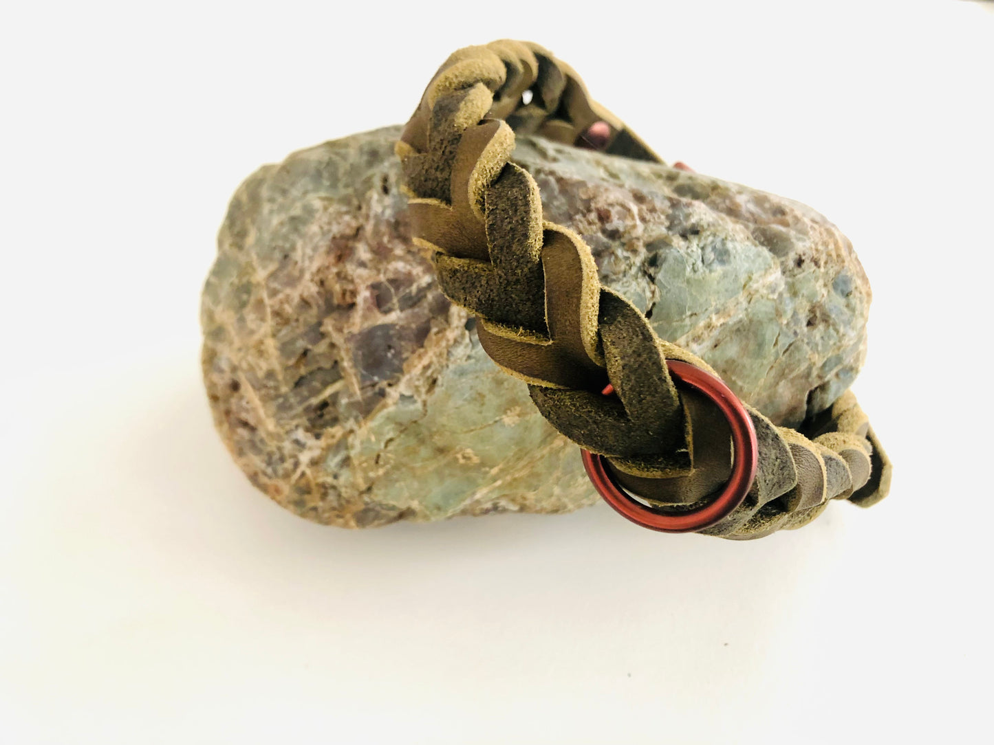 Halsband in Olive aus Leder geflochten mit schokofarbenen Beschlägen an einen Stein gelehnt
