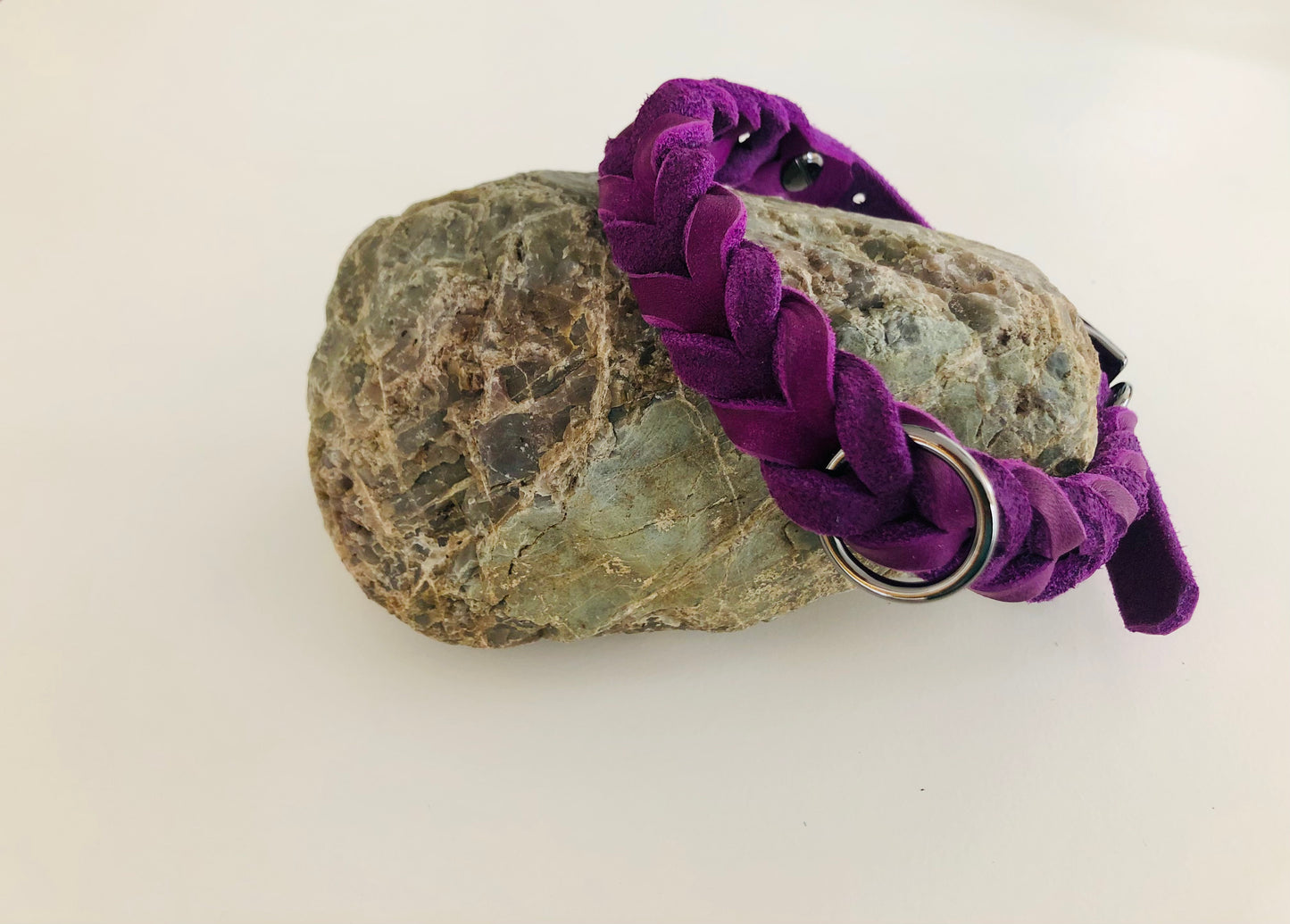 Halsband in Lila aus Leder geflochten mit Verschluß und Ring in Anthrazit an einen Stein gelehnt