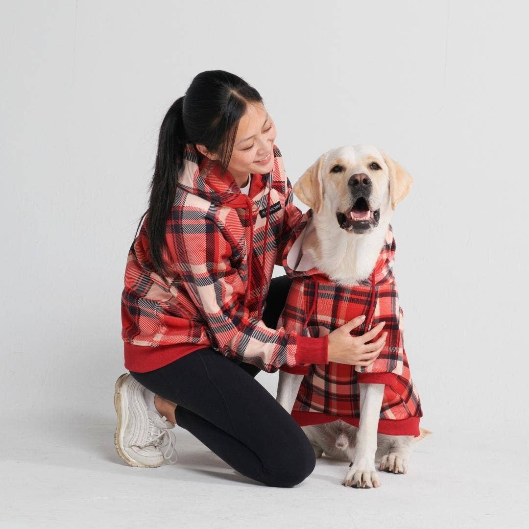 Heller Labrador mit Hundepullover mit Karomuster in den Farben rot, schwarz und weiß und Frau im selben Hoodie,
